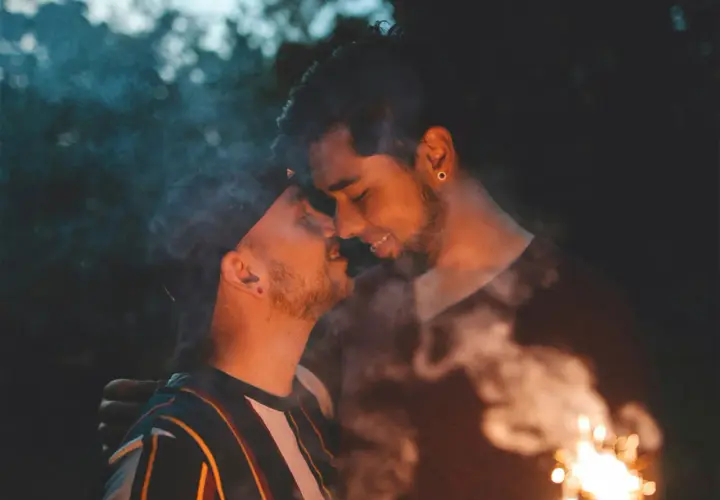 Coppia gay che si bacia con scintille e fumo, un momento intimo e passionale.