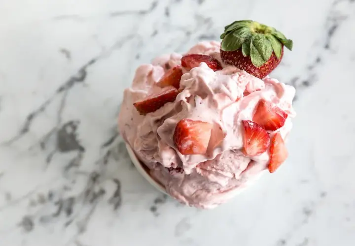 Un délice rose et crémeux : un sorbet fraise garni de morceaux de fruits frais et d'une fraise entière sur un fond marbré.