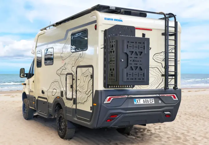 Camping-car Eura Mobil Xtura sur une plage de sable, avec une échelle arrière et un porte-roue noir.
