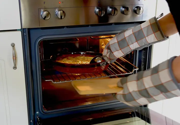 Mit Ofenhandschuhen wird ein Auflauf aus dem Backofen mit Umluft genommen.
