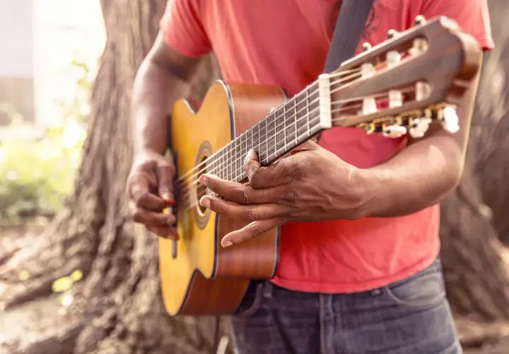 Uomo suona chitarra acustica all'aperto, ideale per imparare canzoni in inglese con testo facile.