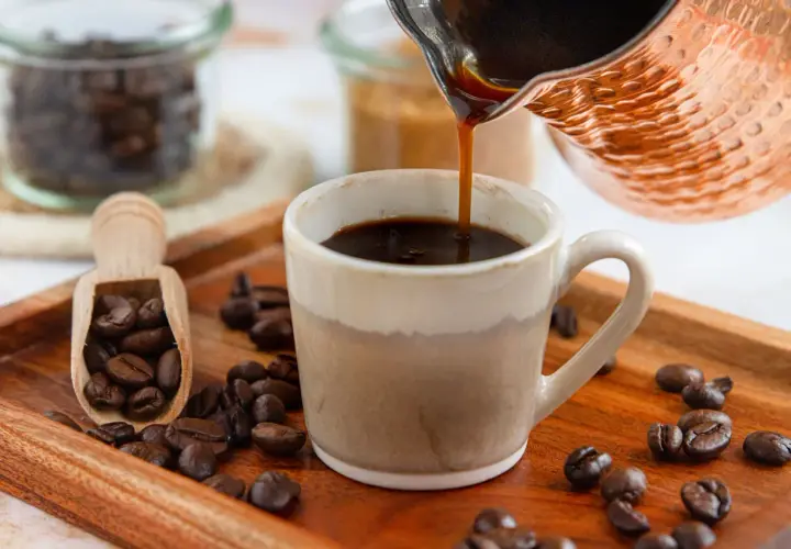 Frisch aufgebrühter türkischer Mokka fließt in eine Tasse. Kaffeebohnen liegen auf einem Holztablett.