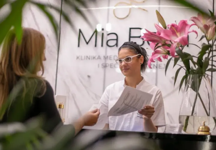 Recepcjonistka w klinice dermatologicznej podaje dokumenty klientce.