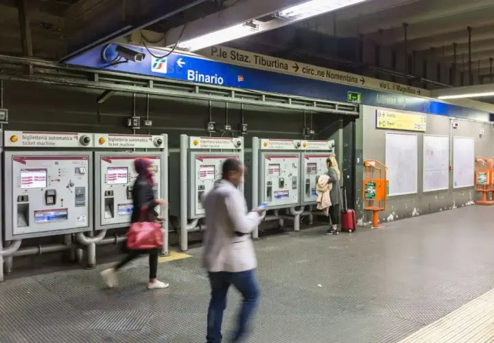 Persone acquistano biglietti alle macchinette automatiche nella stazione metro Roma EUR. Segnali indicano binari e uscite.