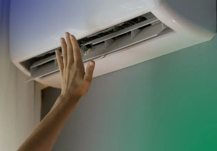 Dłoń dotyka otwartej klimatyzacji ściennej.