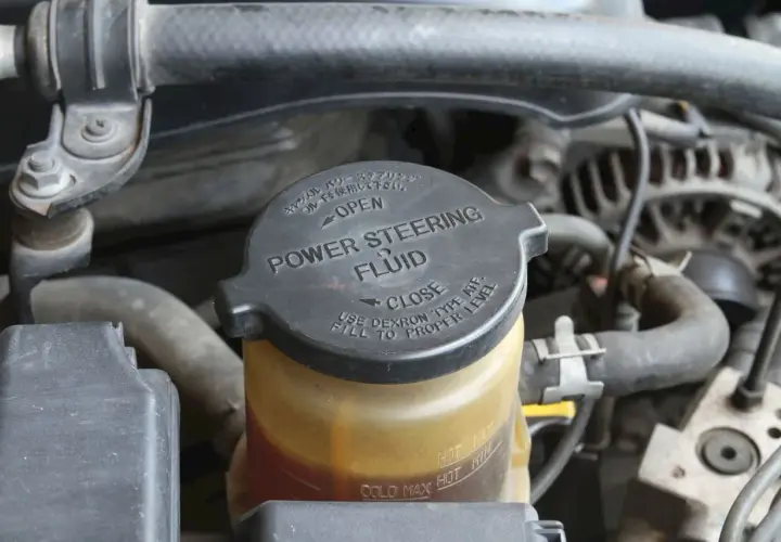 Depósito de líquido de dirección asistida. La tapa negra indica "POWER STEERING FLUID" y las marcas de nivel.