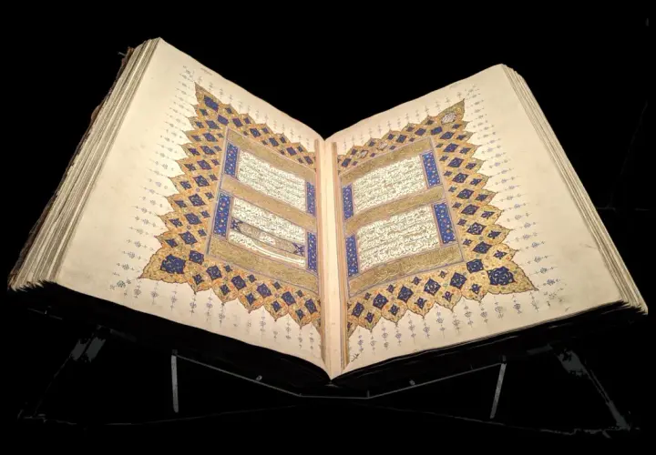 En öppen, gammal Koran på ett ställ, med detaljerad kalligrafi och gyllene ornament. En påminnelse om vem som skrev Koranen.