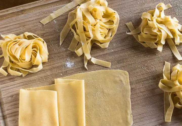 Frischer, selbstgemachter Pastateig, wie im original italienischen Rezept, liegt auf einem Holzbrett. Tagliatelle-Nester und Teigplatten warten auf ihre Zubereitung.