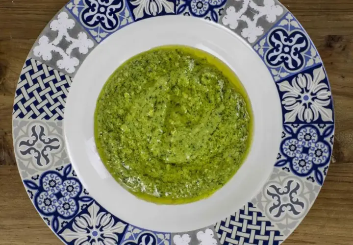 Un plato blanco con un vibrante pesto genovese, adornado con un borde de azulejos azules y grises.