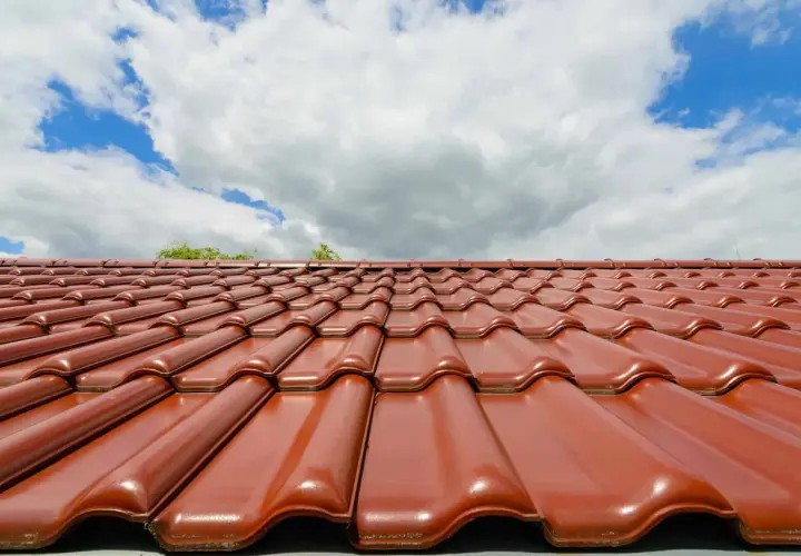 Czerwona dachówka ceramiczna lśni w słońcu. Zastanawiasz się, jaka dachówka ceramiczna najlepsza? Ta prezentuje się okazale.