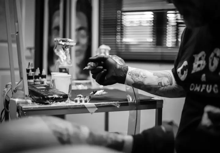 Artysta tworzy skomplikowany ornament tattoo na ręce klienta. Widać maszynkę, tusze i przygotowania do sesji.