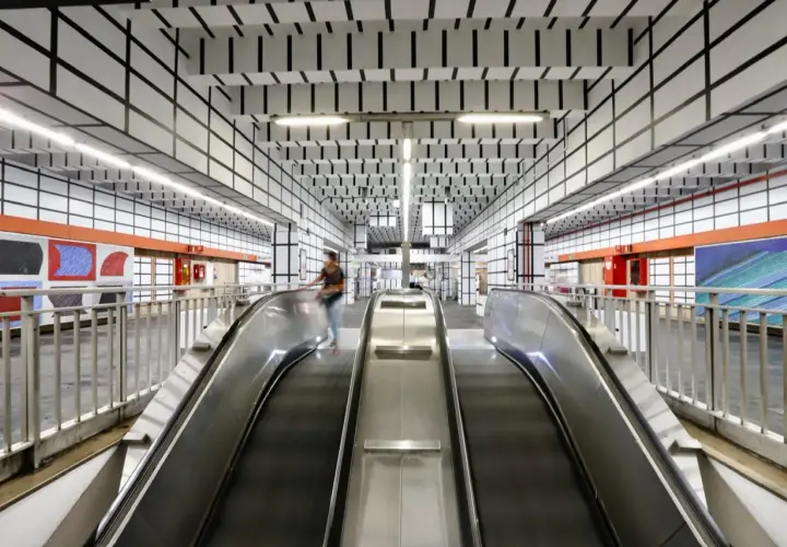 Scale mobili nella moderna stazione metro Vittorio Emanuele a Roma, con soffitto a griglia nera su bianco e opere d'arte colorate alle pareti.