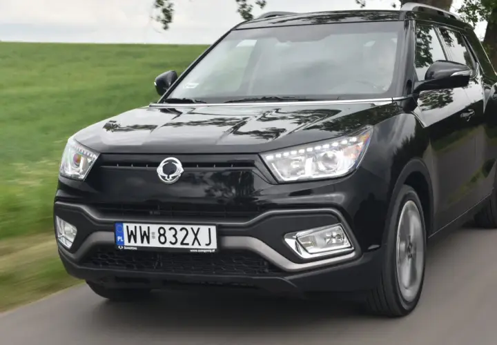 Czarny SsangYong Tivoli, model suw 2000, pędzi po wiejskiej drodze wśród zielonych pól.