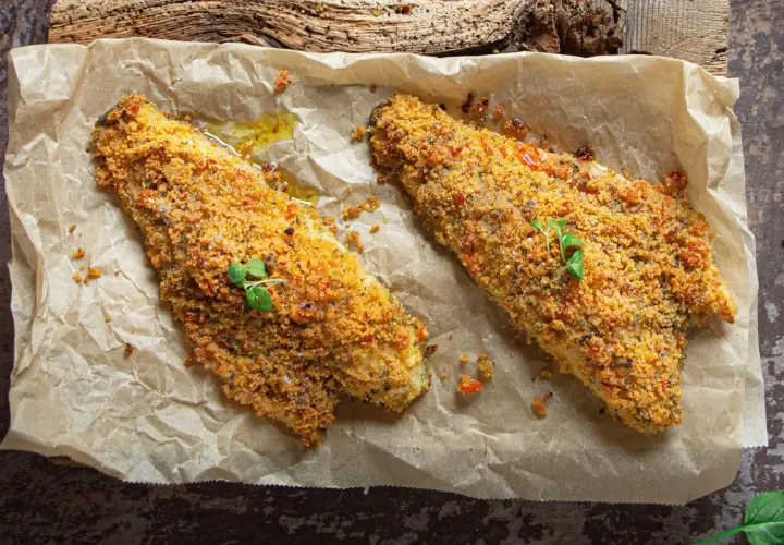 Filetti di orata in padella gratinati, dorati e croccanti, guarniti con erbe fresche.