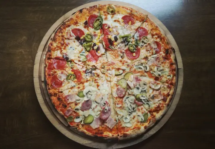 Apetyczna pizza na cienkim cieście z różnymi dodatkami: salami, pieczarki, kukurydza, papryczki jalapeno i ogórek. Zastanawiasz się, ile kalorii ma pizza na cienkim cieście?