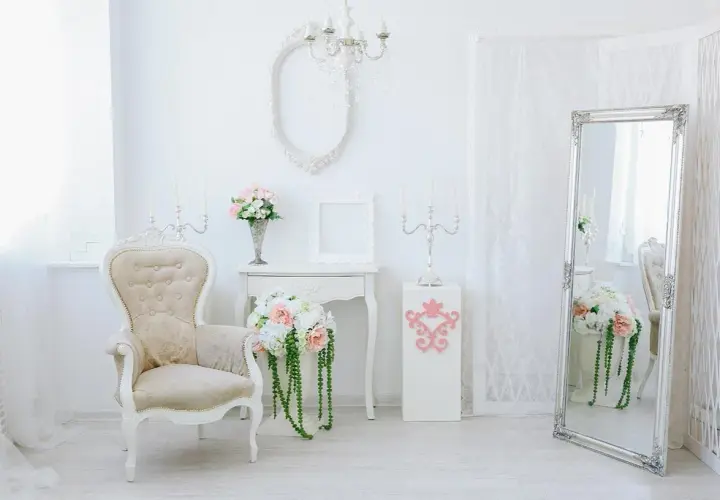 Eleganckie wnętrze w stylu shabby chic: kremowa sofa, wazon z kwiatami, lustro i świeczniki tworzą romantyczną atmosferę.