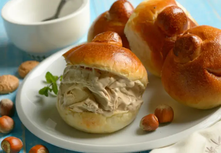 Brioche col tuppo ripieno di gelato, con nocciole e biscotti intorno.