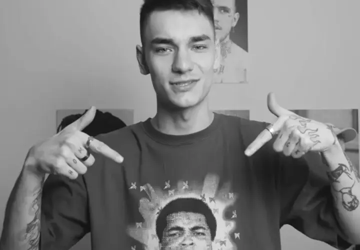 Młody youtuber w koszulce z Muhammadem Alim, z tatuażami na rękach, wskazuje na siebie.