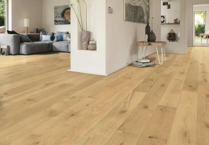Un soggiorno moderno con parquet chiaro. Un divano grigio e un tavolino completano l'arredamento. Immagine che illustra come si monta il parquet.