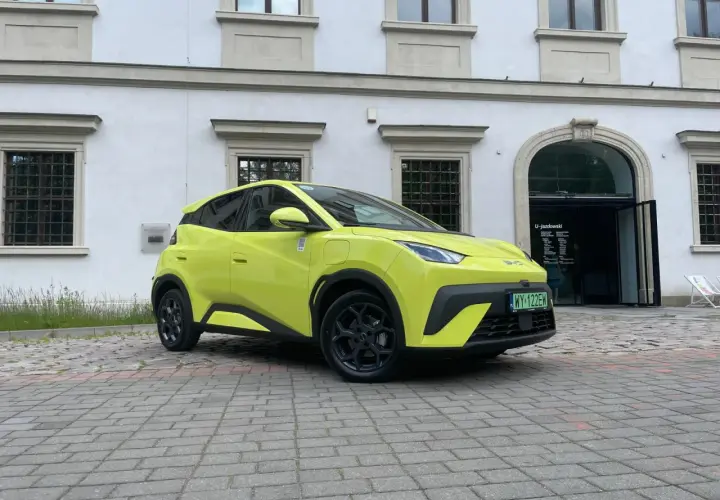 Jaskrawożółty BYD Seagull zaparkowany na bruku przed budynkiem z łukowym wejściem.
