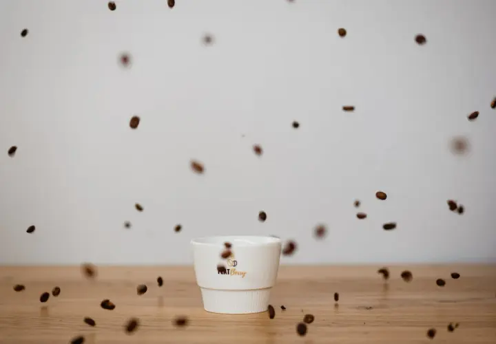 Kaffeebohnen tanzen um eine weiße Tasse. Der Duft verspricht vollen Kaffee Geschmack.