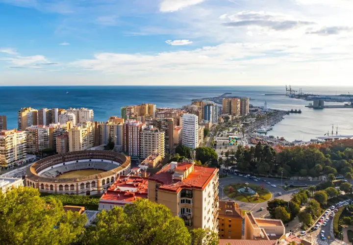 Malaga, listopad: słoneczna pogoda nad miastem, morzem i portem. Widoczna arena, budynki mieszkalne i park.