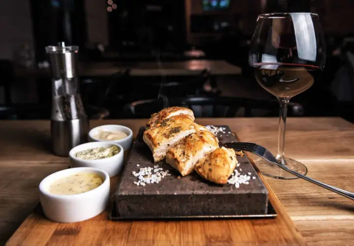 Un plat de poulet grillé avec trois sauces, du sel, un moulin à poivre et un verre de vin rouge. La question est : quel vin avec viande blanche ?