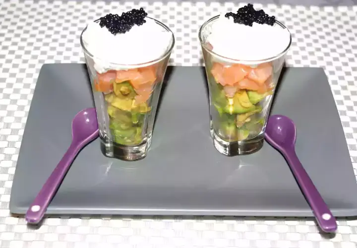 Deux verrines avocat saumon, garnies de crème et de caviar, prêtes à être dégustées avec leurs cuillères violettes.
