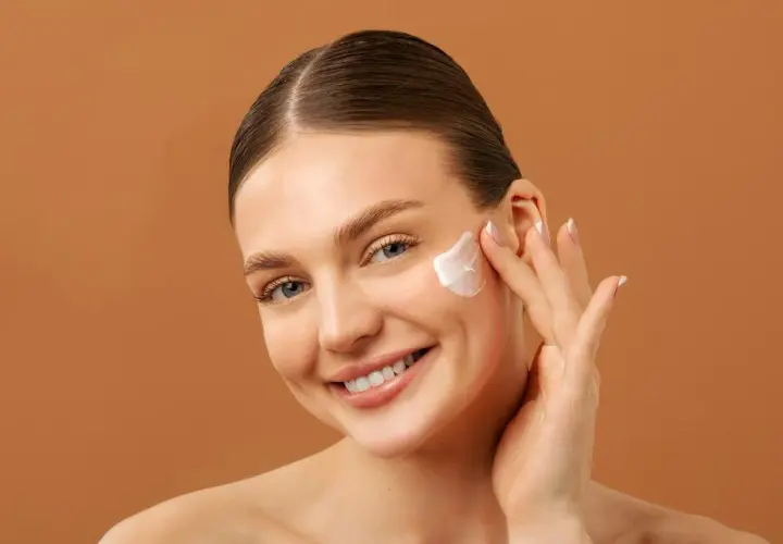 Mujer sonriente aplicándose crema facial. Una rutina de belleza con retinol y vitamina c para una piel radiante.