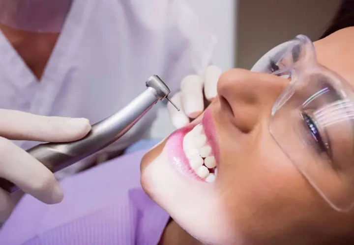 Visita dentistica per rimuovere il tartaro dai denti. La paziente indossa occhiali protettivi mentre il dentista usa uno strumento rotante.