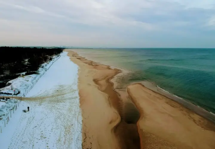 Plaża nad Bałtykiem zimą: śnieg, piasek i turkusowa woda.