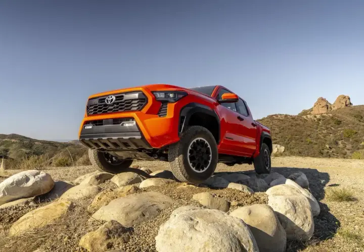 Pomarańczowa Toyota Tacoma pokonuje skalisty teren, gotowa na każdą przygodę.