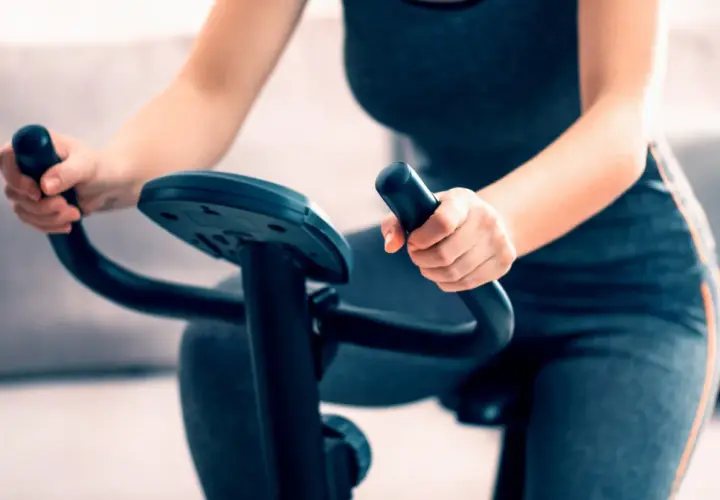 Kobieta wykonuje trening na rowerze stacjonarnym, trzymając kierownicę.