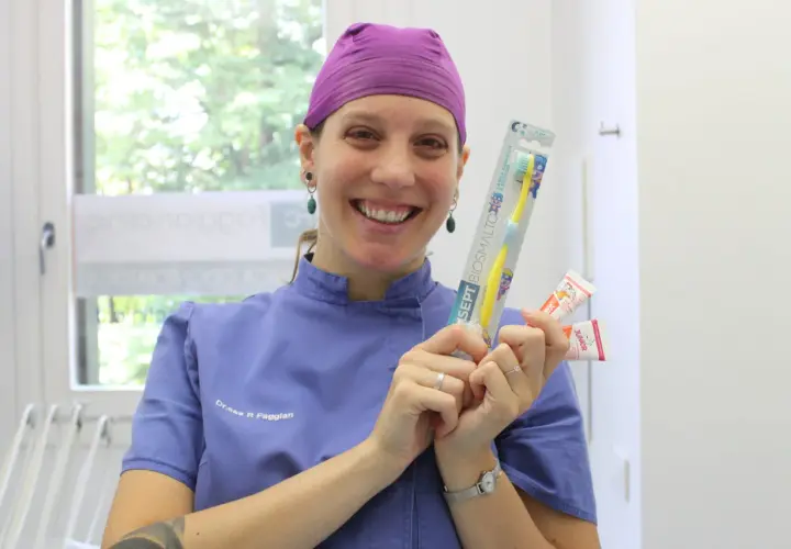 Sorriso di un dentista che mostra spazzolino e dentifrici per la pulizia dei denti bambini.
