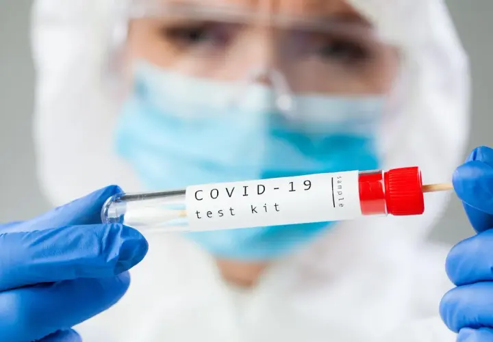 Osoba w kombinezonie ochronnym trzyma probówkę z wymazem. Zastanawiasz się, ile kosztuje test na COVID-19?
