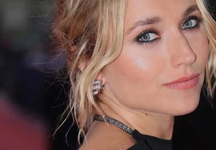 Maquillage yeux bleus d'une blonde, avec des boucles d'oreilles scintillantes et un collier discret.