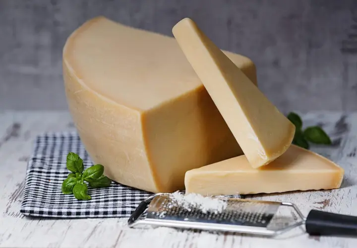 Twardy, żółty ser, przypominający parmezan- polski odpowiednik, leży obok tarki z wiórkami.