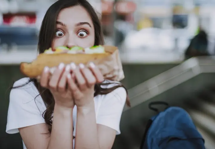 Zaskoczona dziewczyna trzyma duży kebab, zastanawiając się, ile kosztuje.
