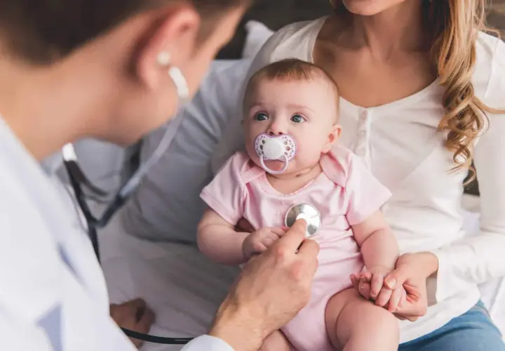 Un médecin examine un bébé avec un stéthoscope, vérifiant les symptômes de la coqueluche.