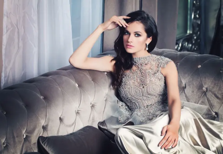 Elegancka kobieta w błyszczącej sukni, uosobienie stylizacji glamour, siedzi na aksamitnej kanapie.