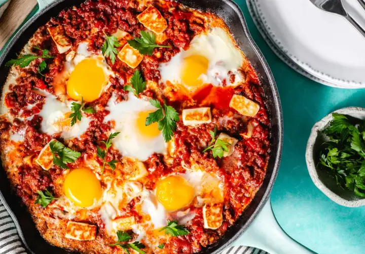 Chakchouka sans poivron : œufs pochés dans une sauce tomate épicée, parsemée de fromage halloumi grillé et de persil frais.