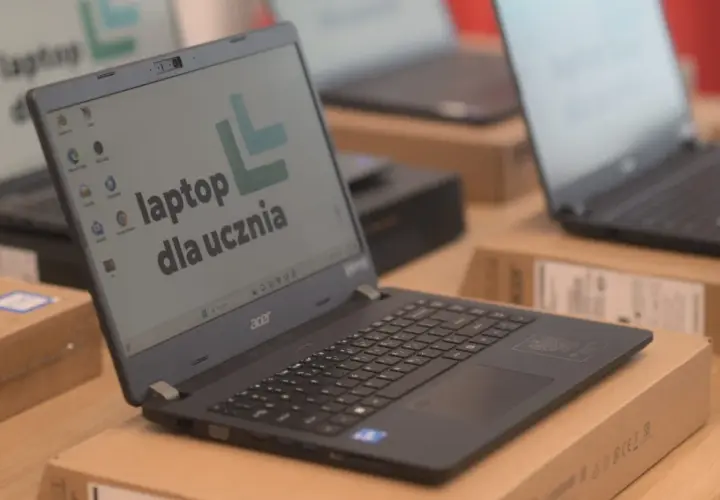 Laptop Acer z napisem "laptop dla ucznia" na ekranie, otoczony innymi laptopami i pudełkami.