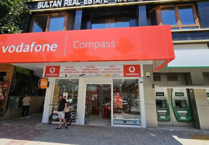Sklep Vodafone z szyldem "Compass", bankomaty i lodówka Coca-Cola.