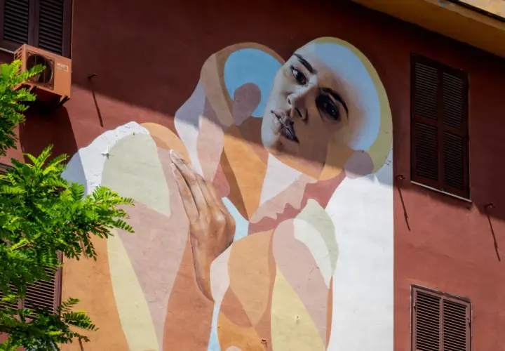 Un volto intenso e mani giunte su un muro colorato in via di Tor Marancia, un'opera d'arte che cattura lo sguardo.