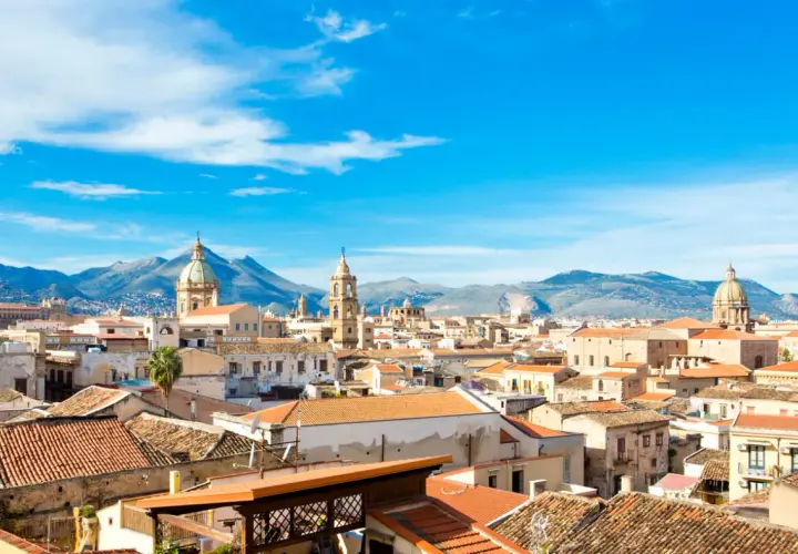 Palermo, luty. Słoneczna pogoda nad dachem miasta, w tle góry i błękitne niebo z chmurami.