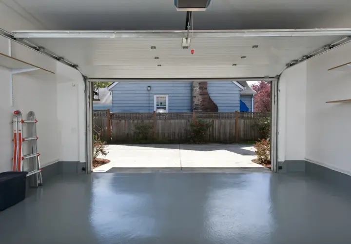 Interno di un garage con porta sezionale aperta su un cortile. Si vede una scala e un contenitore. Pensare a quanto costa trasformare un garage in abitazione.