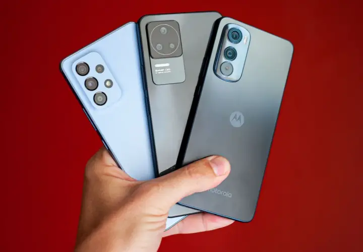 Dłoń trzyma trzy smartfony: jasnoniebieski, szary i ciemnoszary z logo Motorola. Kraj pochodzenia tej marki to USA.