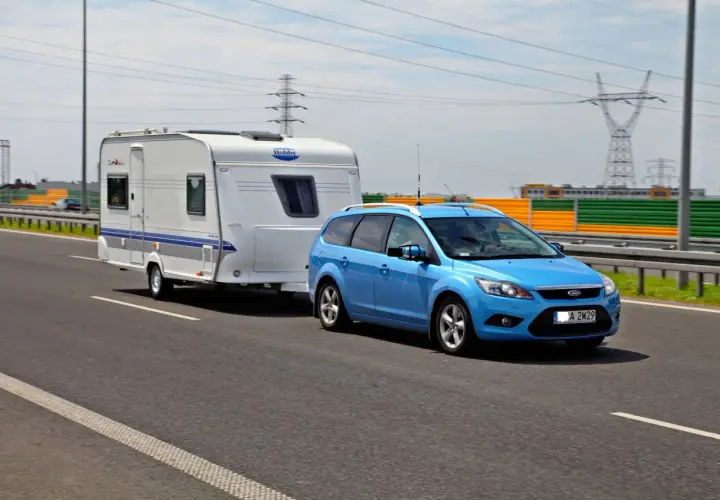 Niebieski Ford Focus z przyczepą kempingową Hobby na drodze. Zestaw mieści się w limitach maksymalna długość pojazdu z przyczepą kat b.