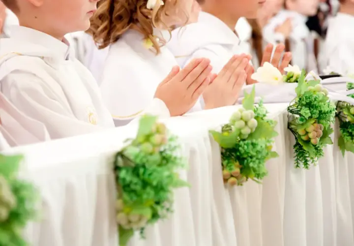 Dzieci w bieli, z modlącymi się dłońmi, czekają na komunię. Dekoracje z winogron i zieleni podkreślają uroczystość, a koszty komunii w kościele są nieodłącznym elementem tego dnia.