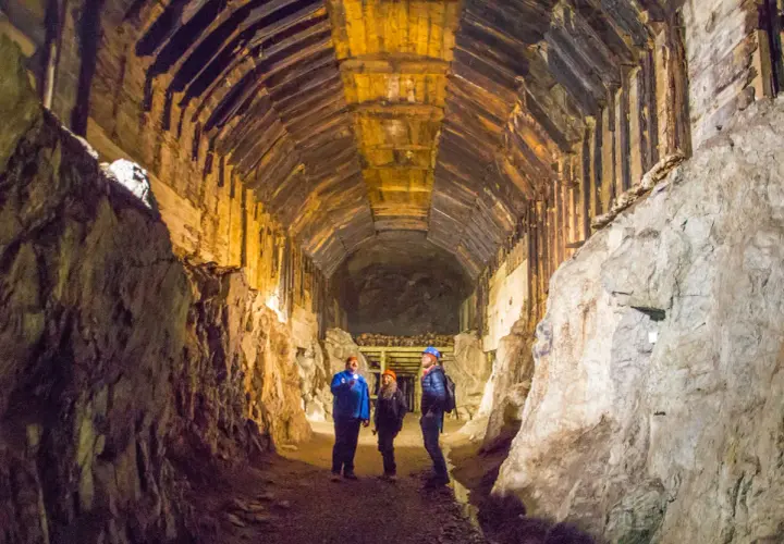 Trzech turystów z latarkami eksploruje mroczny tunel kopalni. Czy to osówka czy włodarz, trudno stwierdzić w tym labiryncie.